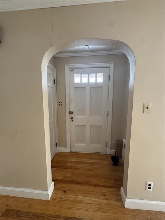 doorway featuring arched walkways, light wood finished floors, ornamental molding, and baseboards