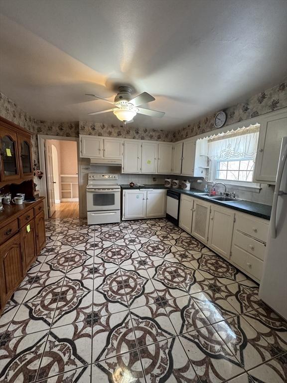 kitchen with white appliances, a sink, white cabinets, dark countertops, and wallpapered walls