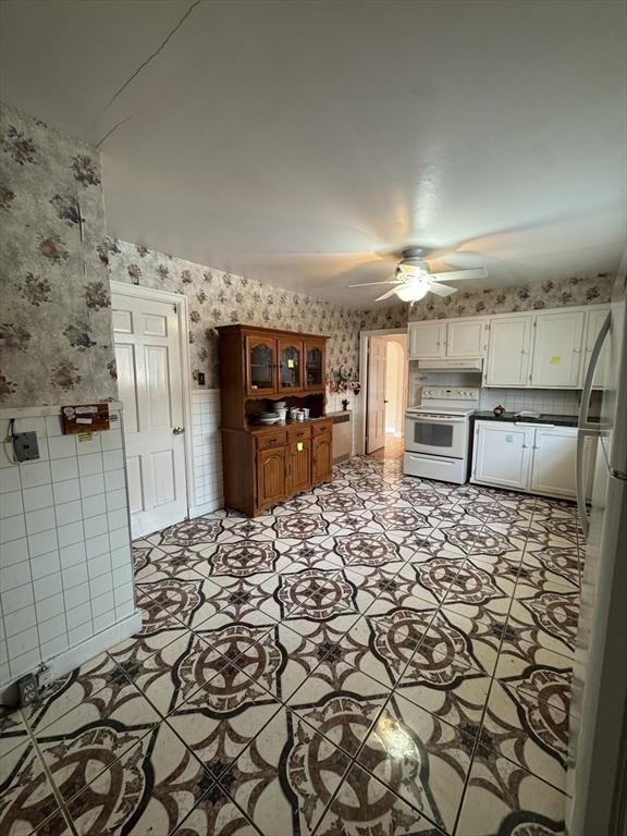 kitchen featuring white range with electric cooktop, a ceiling fan, white cabinets, under cabinet range hood, and wallpapered walls