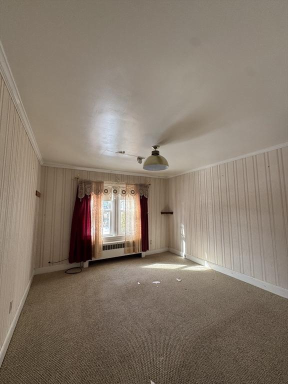 carpeted spare room with baseboards, crown molding, and radiator heating unit