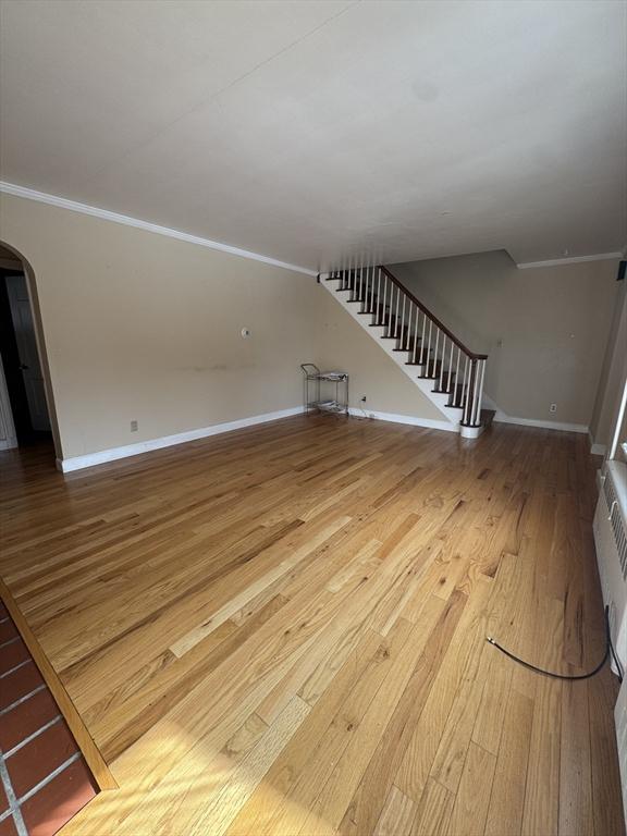 unfurnished living room featuring baseboards, arched walkways, stairway, wood finished floors, and crown molding