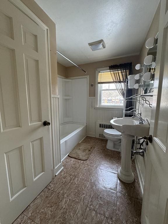 full bath featuring toilet, radiator heating unit, wainscoting, tub / shower combination, and a textured ceiling