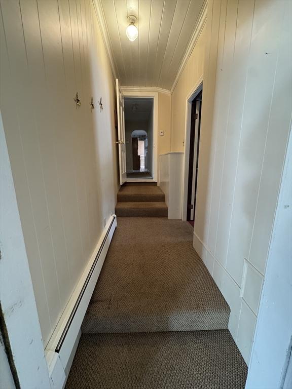 hallway featuring a baseboard heating unit, ornamental molding, dark carpet, and a decorative wall