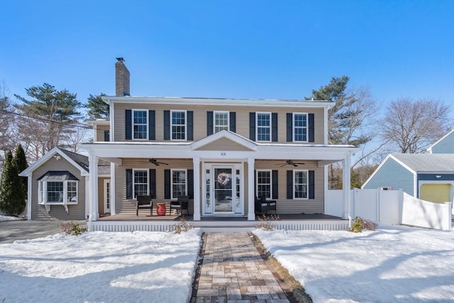 colonial inspired home featuring ceiling fan, a chimney, covered porch, and fence