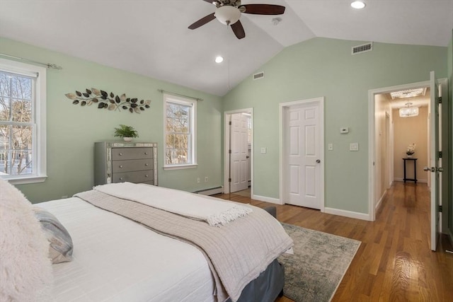 bedroom with lofted ceiling, a baseboard heating unit, wood finished floors, and visible vents