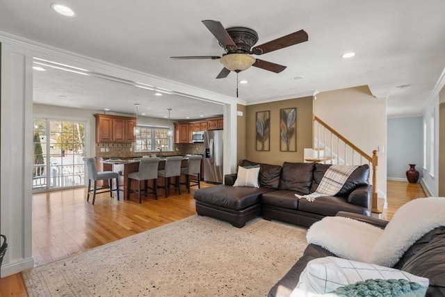 living area featuring light wood finished floors, recessed lighting, ornamental molding, a ceiling fan, and stairs