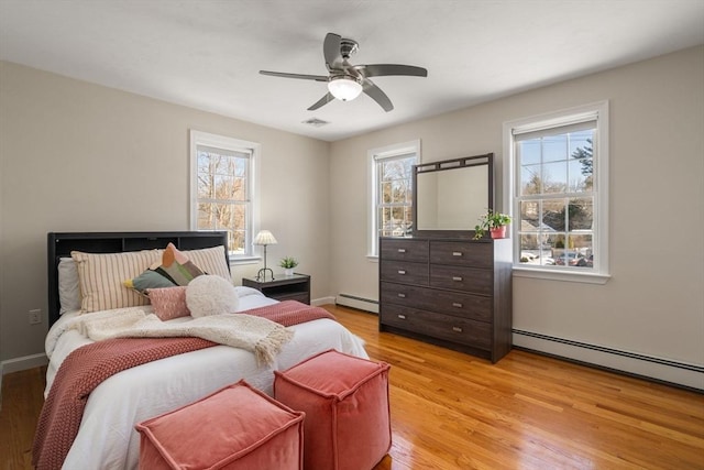 bedroom with a baseboard heating unit, light wood-type flooring, multiple windows, and baseboards