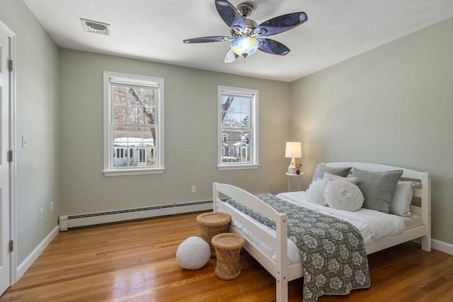 bedroom with visible vents, a baseboard heating unit, a ceiling fan, wood finished floors, and baseboards