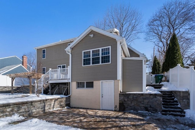 snow covered property with a chimney, fence, stairway, and a deck