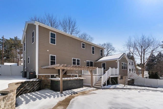 snow covered house with stairway, cooling unit, fence, and a pergola