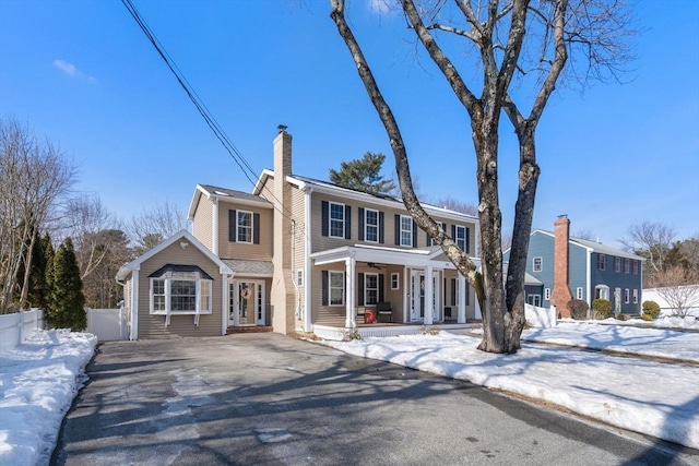 colonial home featuring covered porch, aphalt driveway, a chimney, and fence