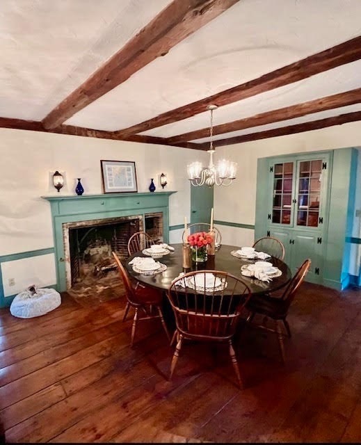 dining area with a chandelier, beamed ceiling, wood-type flooring, and a fireplace