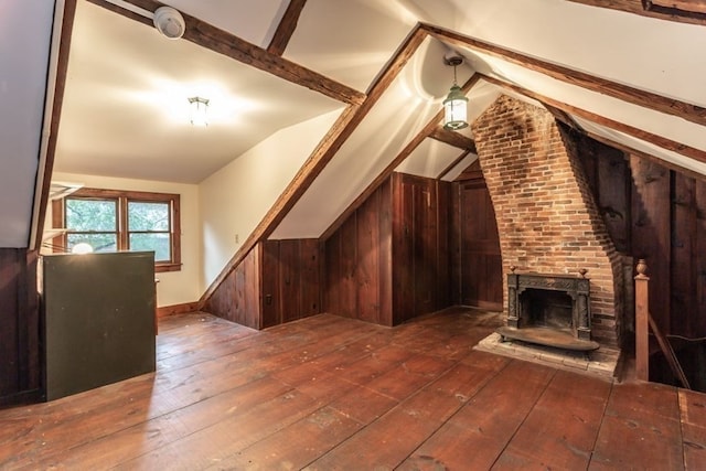 additional living space with a brick fireplace, wood walls, lofted ceiling with beams, and dark hardwood / wood-style flooring