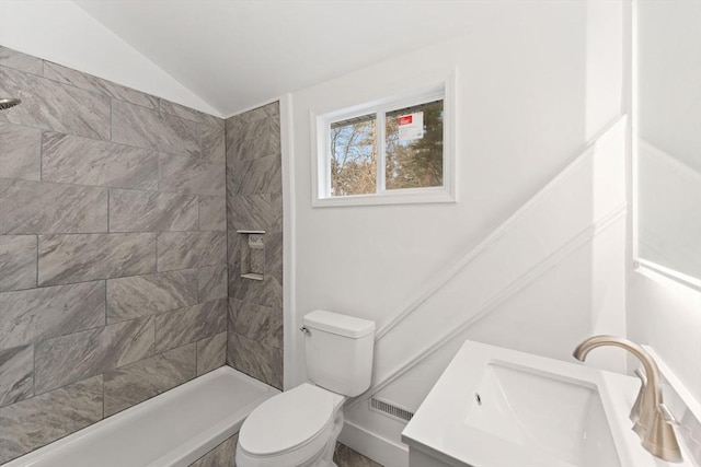 bathroom featuring toilet, vaulted ceiling, tiled shower, and vanity