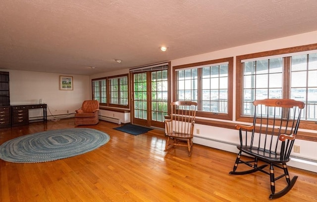 living area with a baseboard radiator, light wood-type flooring, and a textured ceiling