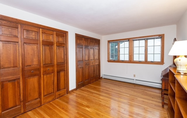 unfurnished bedroom featuring light hardwood / wood-style floors, two closets, and a baseboard heating unit