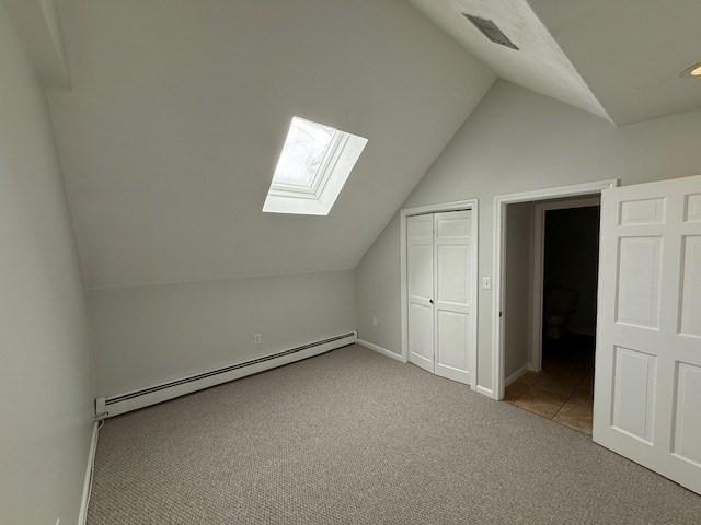 additional living space featuring light carpet, a baseboard radiator, lofted ceiling, and visible vents