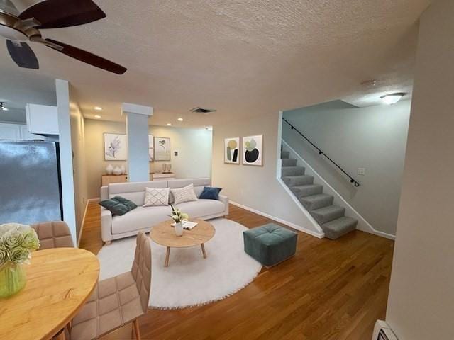 living area featuring light wood finished floors, baseboards, a ceiling fan, stairway, and a textured ceiling