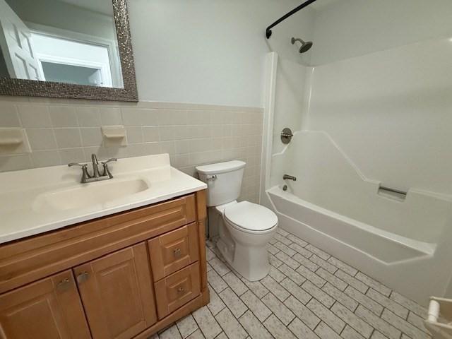 full bath with toilet, a wainscoted wall, vanity, tile walls, and shower / washtub combination