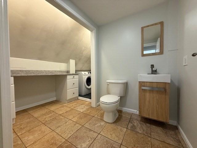 half bathroom featuring baseboards, toilet, lofted ceiling, washer / clothes dryer, and vanity