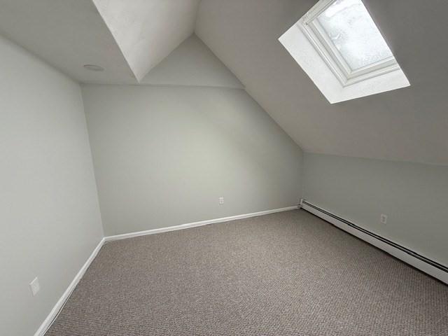 additional living space featuring a baseboard heating unit, baseboards, carpet flooring, and lofted ceiling with skylight