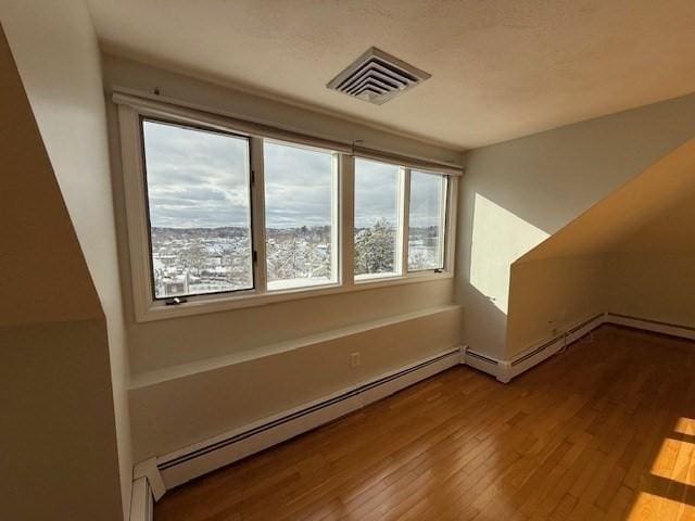 bonus room featuring visible vents, a baseboard heating unit, and wood finished floors