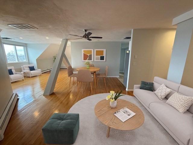 living area with a baseboard radiator, wood finished floors, visible vents, and a ceiling fan