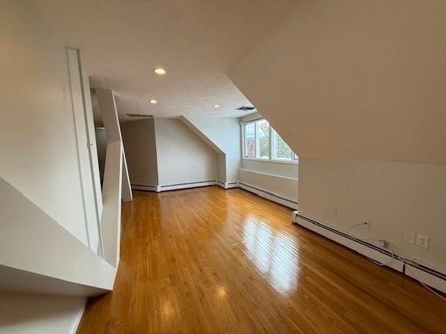 additional living space with lofted ceiling, light wood-style flooring, a baseboard radiator, a baseboard heating unit, and recessed lighting