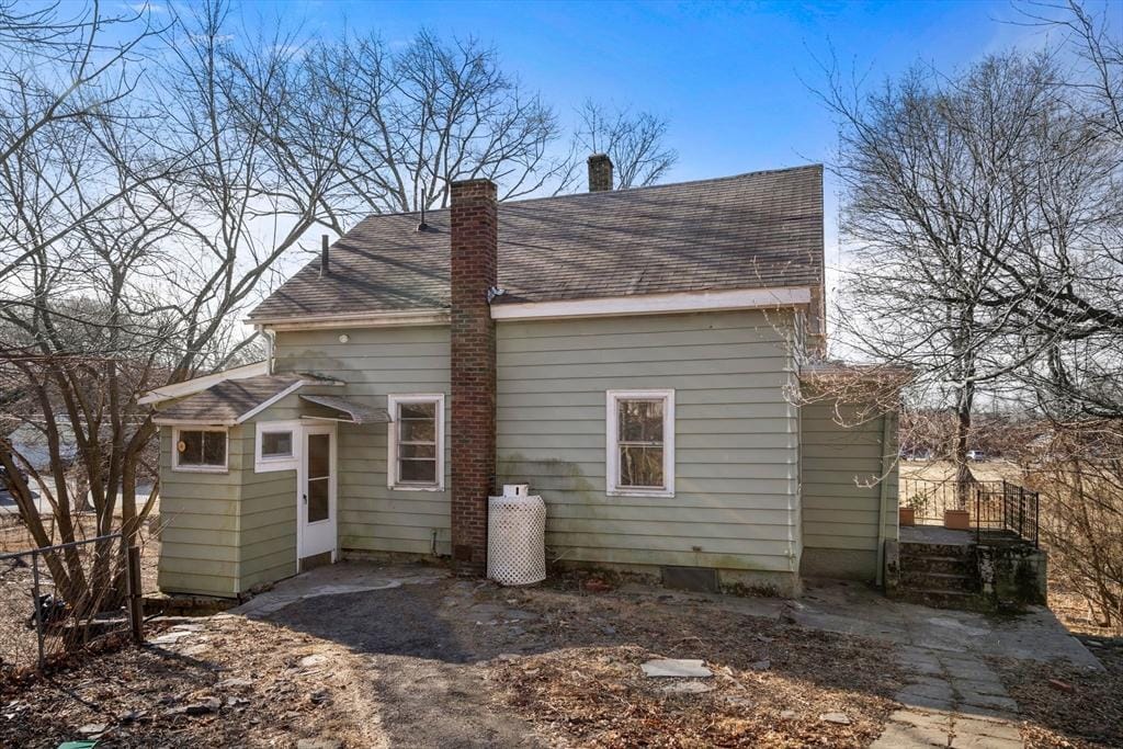back of property with fence, a chimney, and a shingled roof