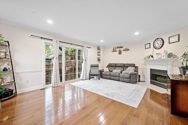 living room featuring wood-type flooring, a fireplace with flush hearth, recessed lighting, and ornamental molding