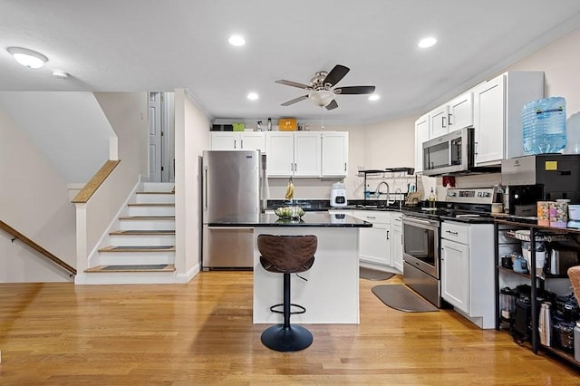 kitchen with stainless steel appliances, a ceiling fan, dark countertops, a kitchen island, and white cabinetry