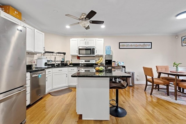 kitchen with stainless steel appliances, a kitchen bar, light wood-style floors, white cabinetry, and crown molding