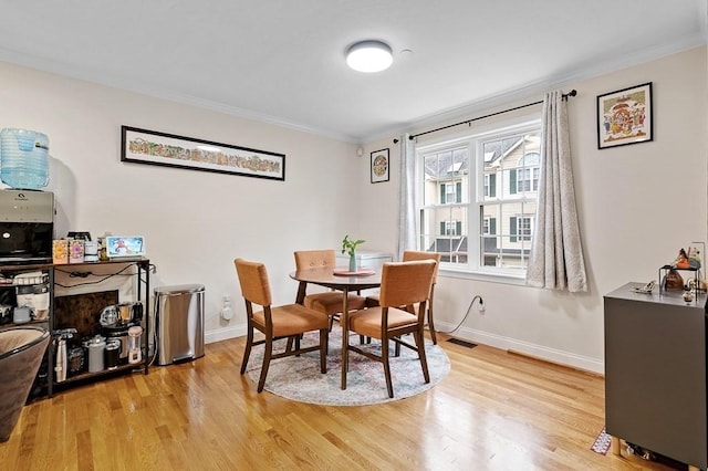 dining space featuring ornamental molding, light wood-style floors, and baseboards