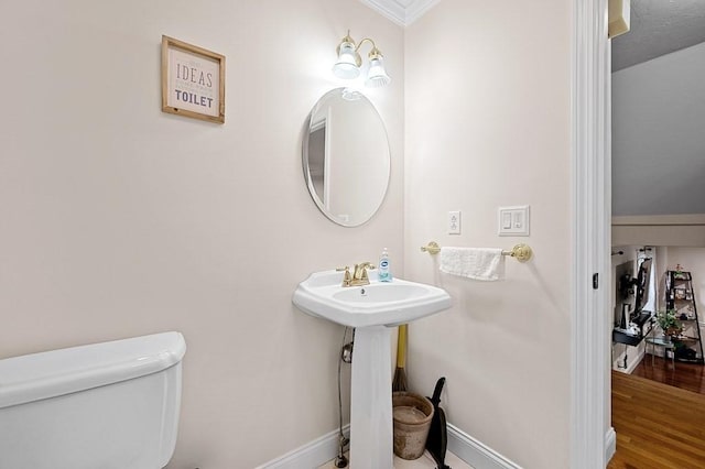 half bath with toilet, baseboards, crown molding, and wood finished floors