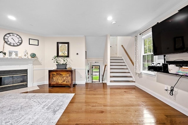 living area featuring stairs, wood finished floors, a glass covered fireplace, baseboards, and recessed lighting