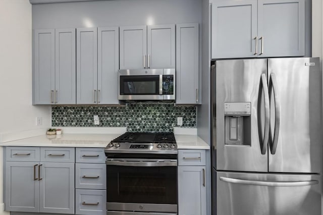 kitchen featuring stainless steel appliances, gray cabinetry, light countertops, and decorative backsplash