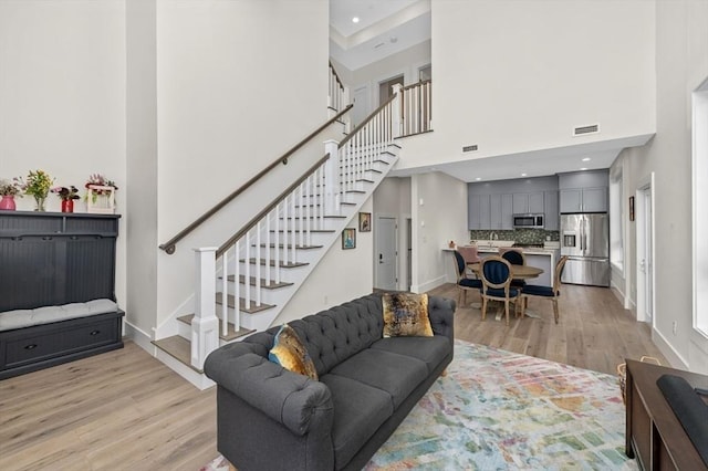 living area featuring light wood-style floors, a towering ceiling, baseboards, and stairs