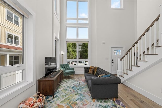 living area featuring a high ceiling, healthy amount of natural light, light wood-style flooring, stairs, and baseboards
