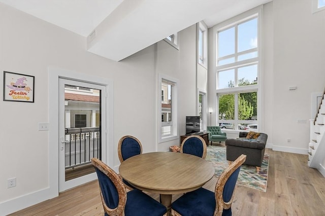 dining space featuring stairway, light wood-style floors, baseboards, and a high ceiling