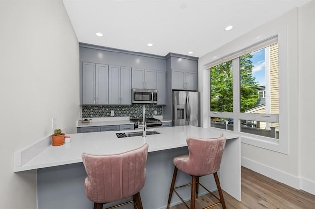kitchen featuring appliances with stainless steel finishes, gray cabinetry, decorative backsplash, wood finished floors, and a kitchen breakfast bar