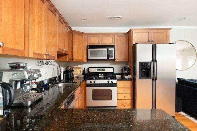 kitchen featuring visible vents, brown cabinets, dark stone countertops, ornamental molding, and stainless steel appliances
