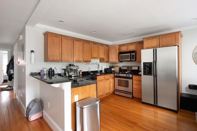 kitchen with dark countertops, brown cabinets, light wood-type flooring, a peninsula, and stainless steel appliances