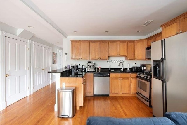 kitchen featuring a sink, appliances with stainless steel finishes, light wood-type flooring, and a peninsula