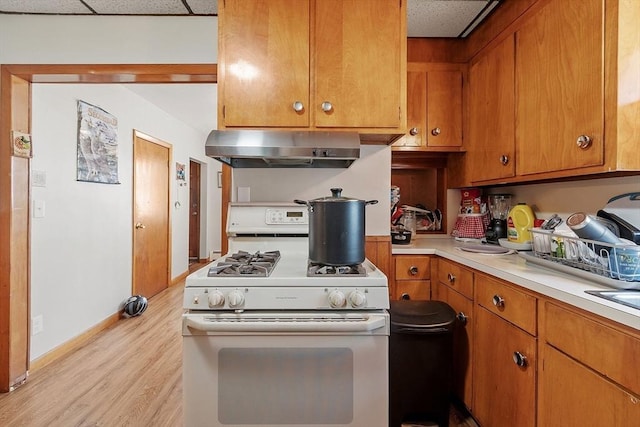 kitchen featuring ventilation hood, white gas stove, light countertops, brown cabinets, and light wood-style floors