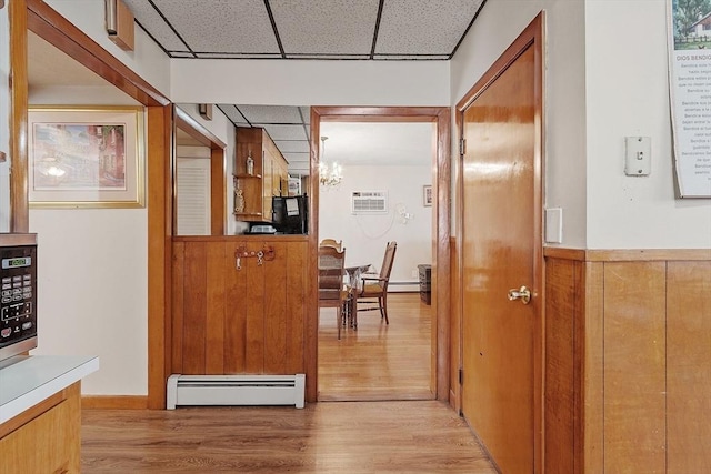 hall featuring a drop ceiling, a baseboard radiator, light wood-style floors, and an inviting chandelier