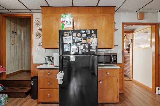 kitchen with stainless steel microwave, a drop ceiling, freestanding refrigerator, light wood-style floors, and brown cabinetry