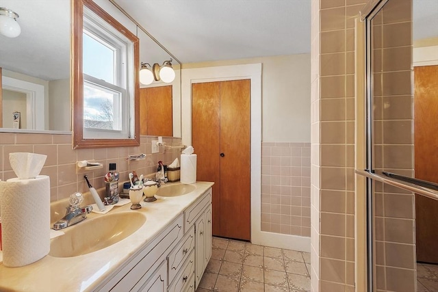 bathroom featuring tile walls, double vanity, a tile shower, and a sink