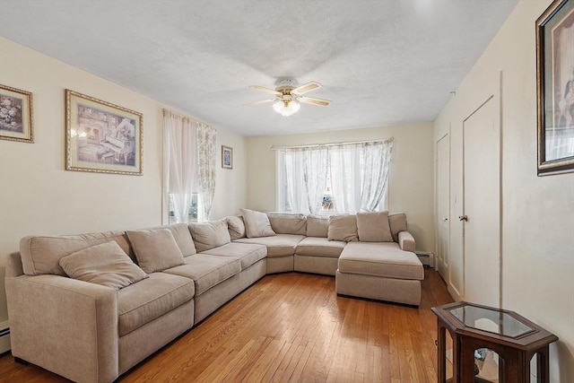 living room with a textured ceiling, light wood-type flooring, ceiling fan, and a baseboard radiator