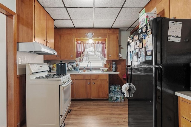 kitchen featuring under cabinet range hood, light countertops, white range with gas cooktop, freestanding refrigerator, and brown cabinetry