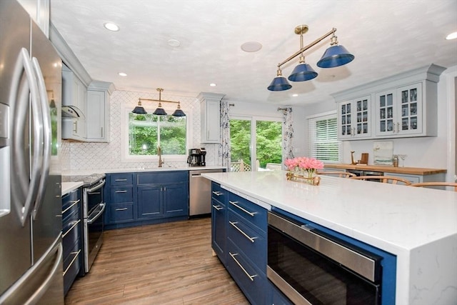 8 Highland View Ave, Mattapoisett, MA 02739 - kitchen featuring stainless steel appliances, blue cabinets, light wood-style floors, decorative backsplash, and hanging light fixtures
